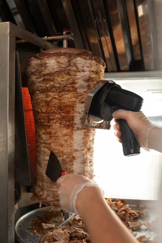 Close-up view of shawarma being sliced with professional equipment in a kitchen.