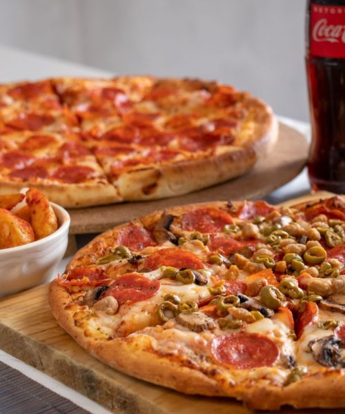 Close-up of pepperoni and veggie pizzas with soda, perfect for a casual dining experience.